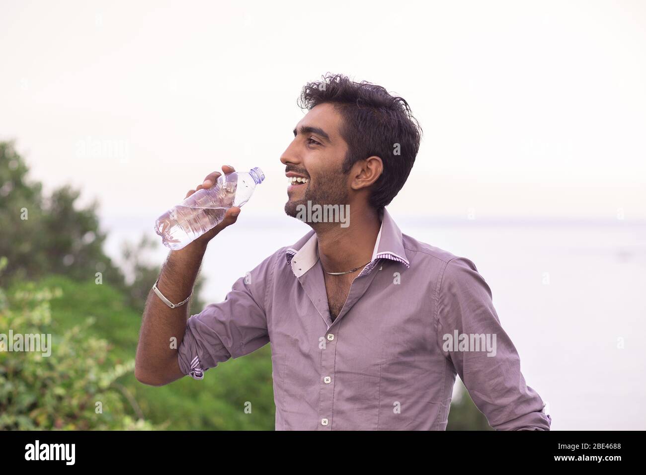 Hydratez-vous. Homme souriant en profil sur le point de boire d'une bouteille d'eau isolé nature arbres et fond de mer Banque D'Images