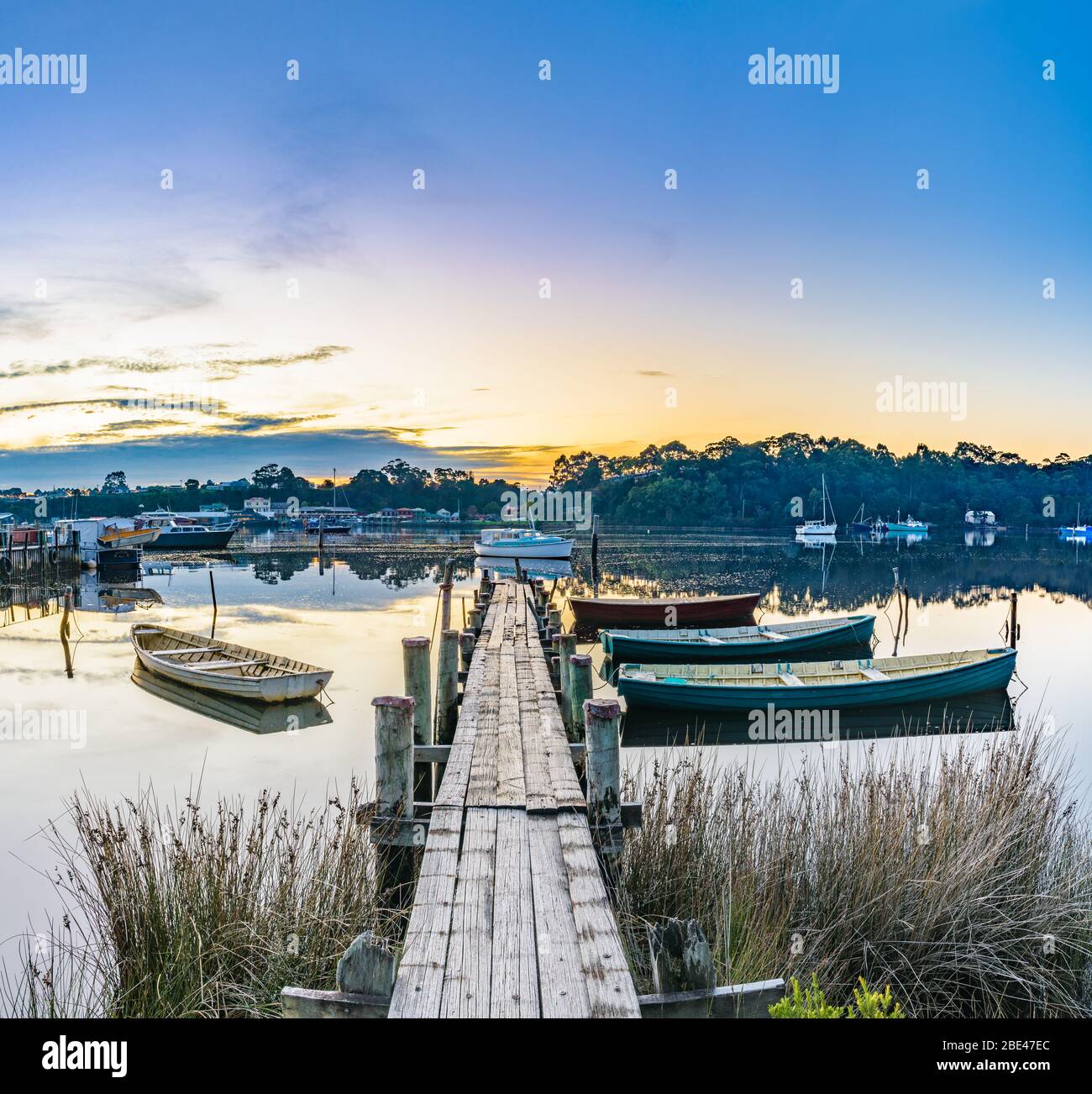Des bateaux traditionnels en bois amarrés à une jetée en bois sur le port de Macquarie avec la ville de Strahan de l'autre côté de la baie en arrière-plan. Banque D'Images