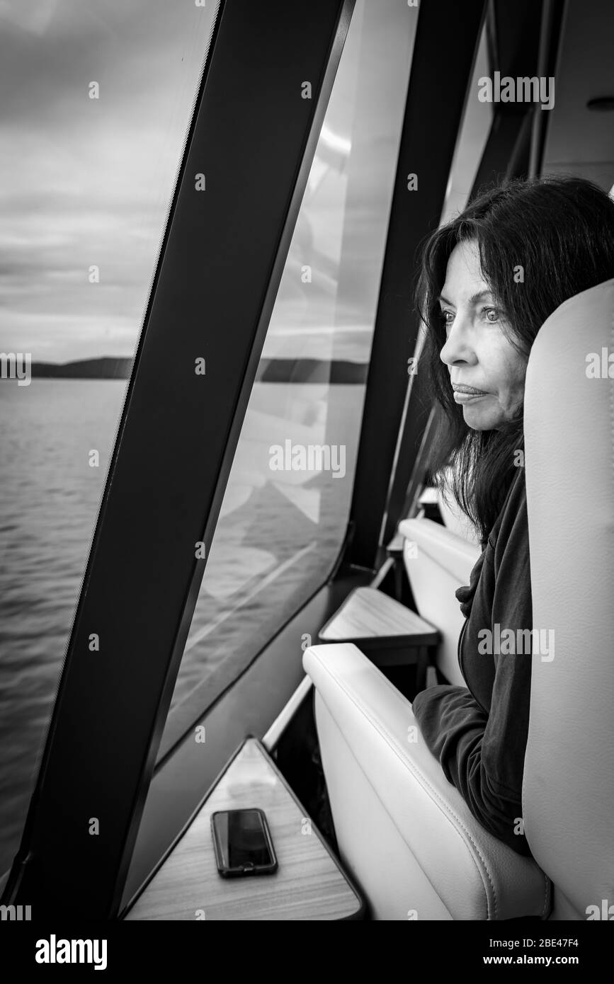 Profil noir et blanc d'une touriste féminine regardant la fenêtre à bord du bateau de croisière Gordon River qui quitte Strahan en Tasmanie. Banque D'Images