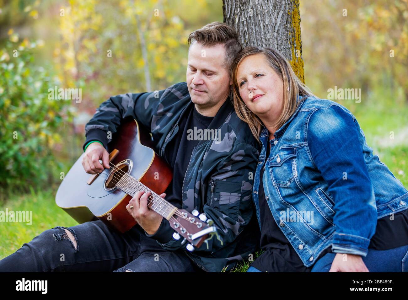 Un couple mûr passant du temps de qualité ensemble et la femme écoute son mari chantant et jouant de sa guitare pendant qu'il est dans un parc de la ville... Banque D'Images