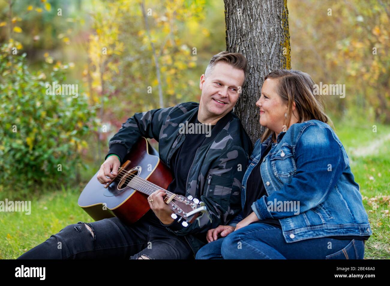Un couple mûr passant du temps de qualité ensemble et la femme écoute son mari chantant et jouant de sa guitare pendant qu'il est dans un parc de la ville... Banque D'Images