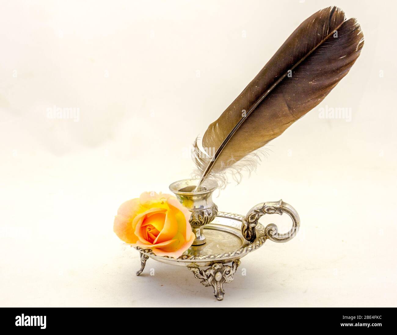 Un inkwell vintage, un stylo plume de quill et une rose orange isolé sur une image d'arrière-plan claire avec espace de copie en format horizontal Banque D'Images