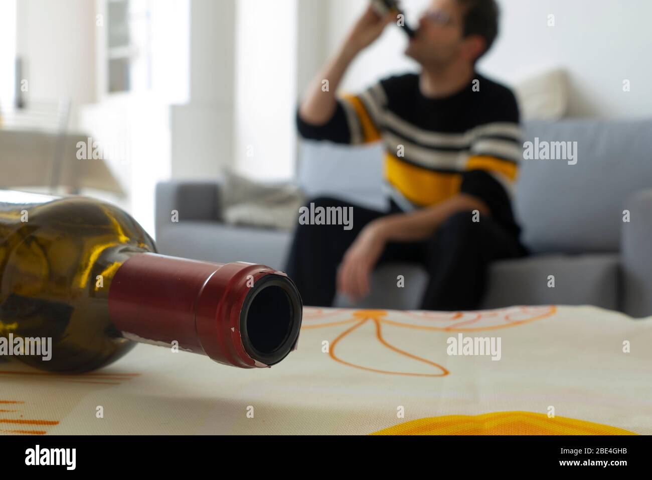 L'alcoolique est bu sur le canapé à la maison en arrière-plan. Bouteille de vin vide au premier plan. Concept de dépendance à l'alcool. Banque D'Images