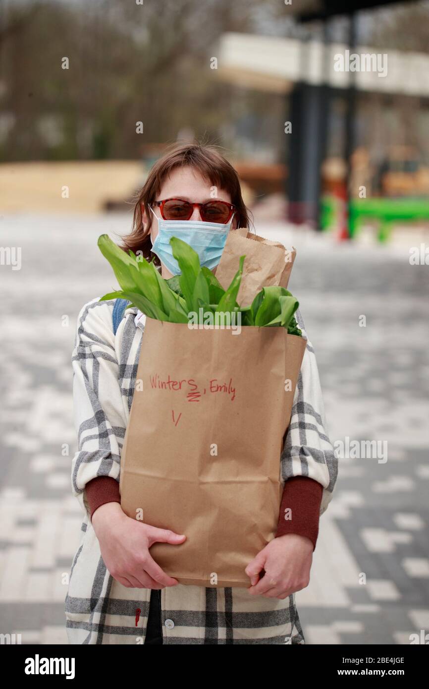 Bloomington, États-Unis. 11 avril 2020. Emily Walters pose pour un portrait, tout en portant un masque facial, après avoir pris sa commande alimentaire, au marché communautaire des agriculteurs de Bloomington, où la nourriture est distribuée dans un arrangement au drive par la première lettre des noms de famille des gens au Pavillon SwitchYard, Les commandes de nourriture ont été prises sur Internet. Crédit: SOPA Images Limited/Alay Live News Banque D'Images