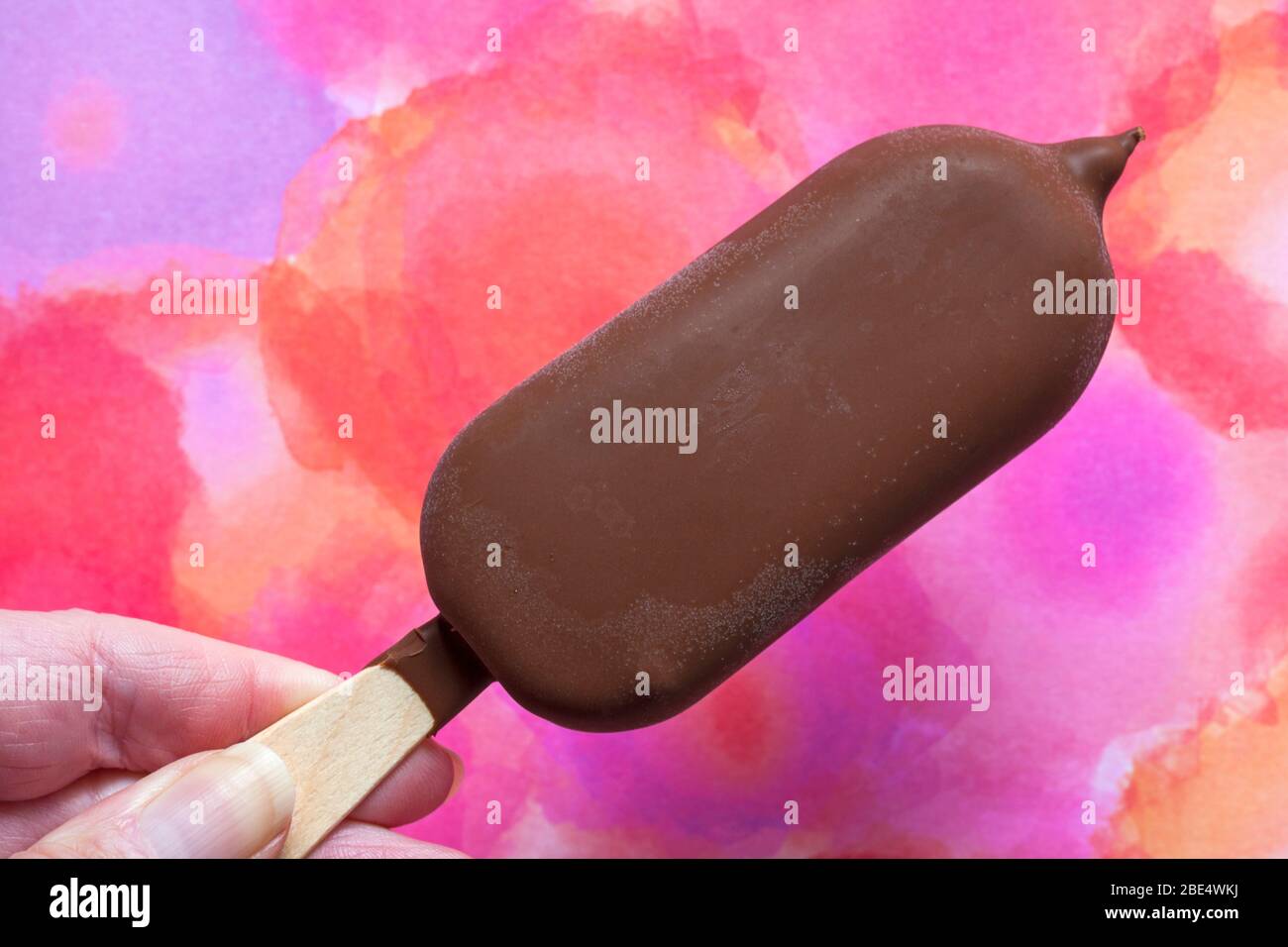 Main tenant Magnum double cerise crème glacée contre fond coloré - Royaume-Uni Banque D'Images
