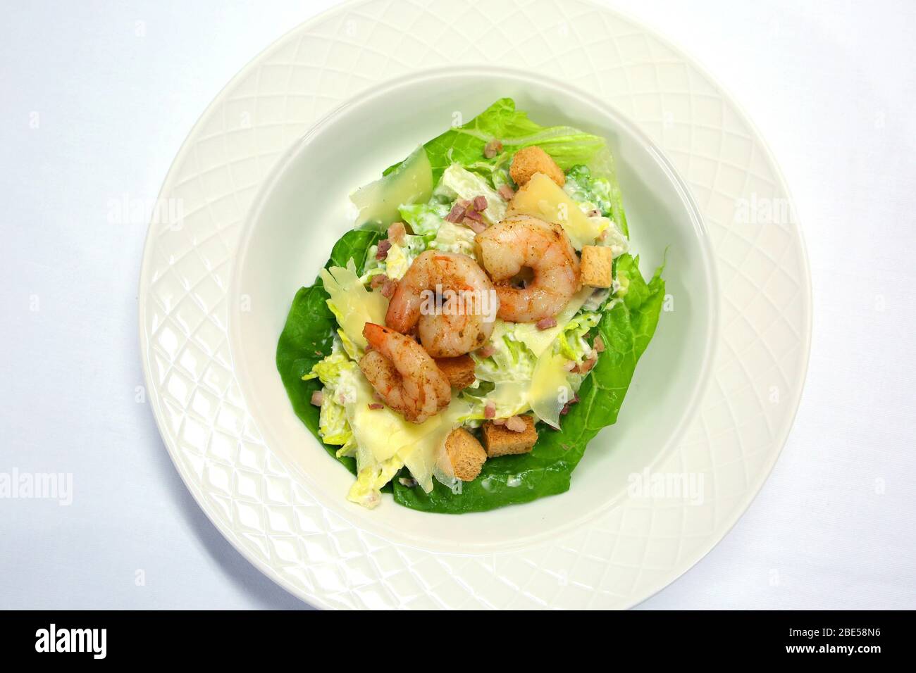 Salade de Ceaser aux crevettes préparées prêtes à manger, servie sur une plaque blanche de chine sur une nappe blanche. Banque D'Images