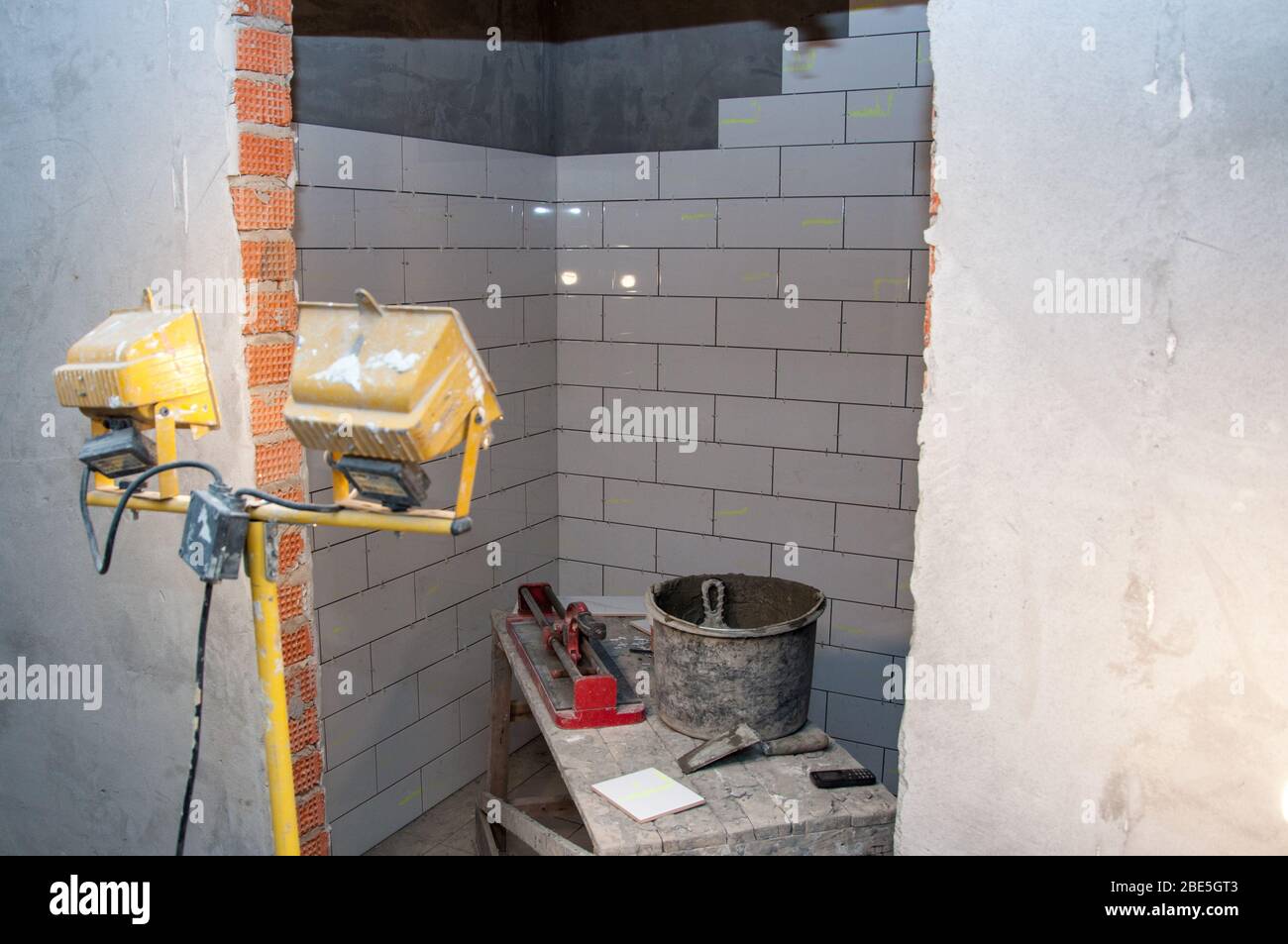 Un projecteur illumine la place d'un travailleur qui pose des tuiles en céramique sur un chantier. Banque D'Images