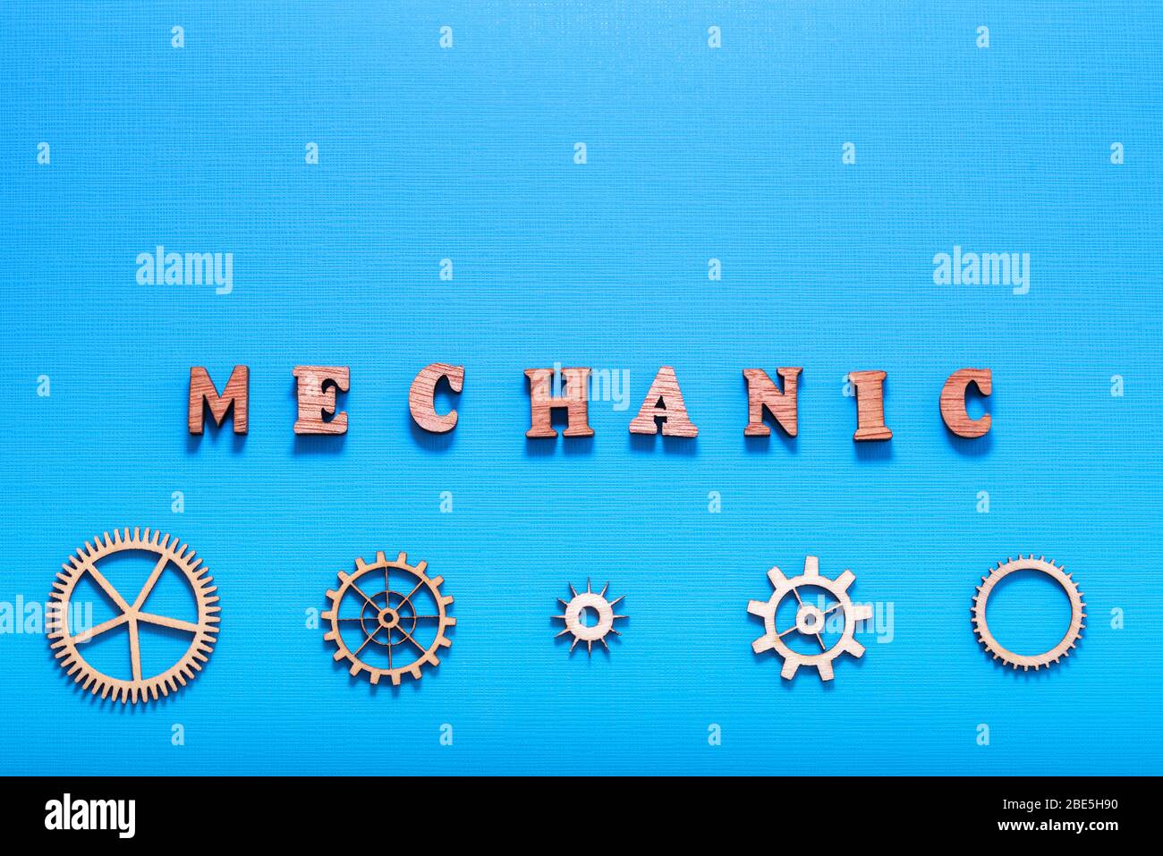 Mot « mécanique » écrit avec des lettres en bois à proximité de pièces de machinerie lourde en bois. Style industriel. Isolé sur fond bleu. Banque D'Images