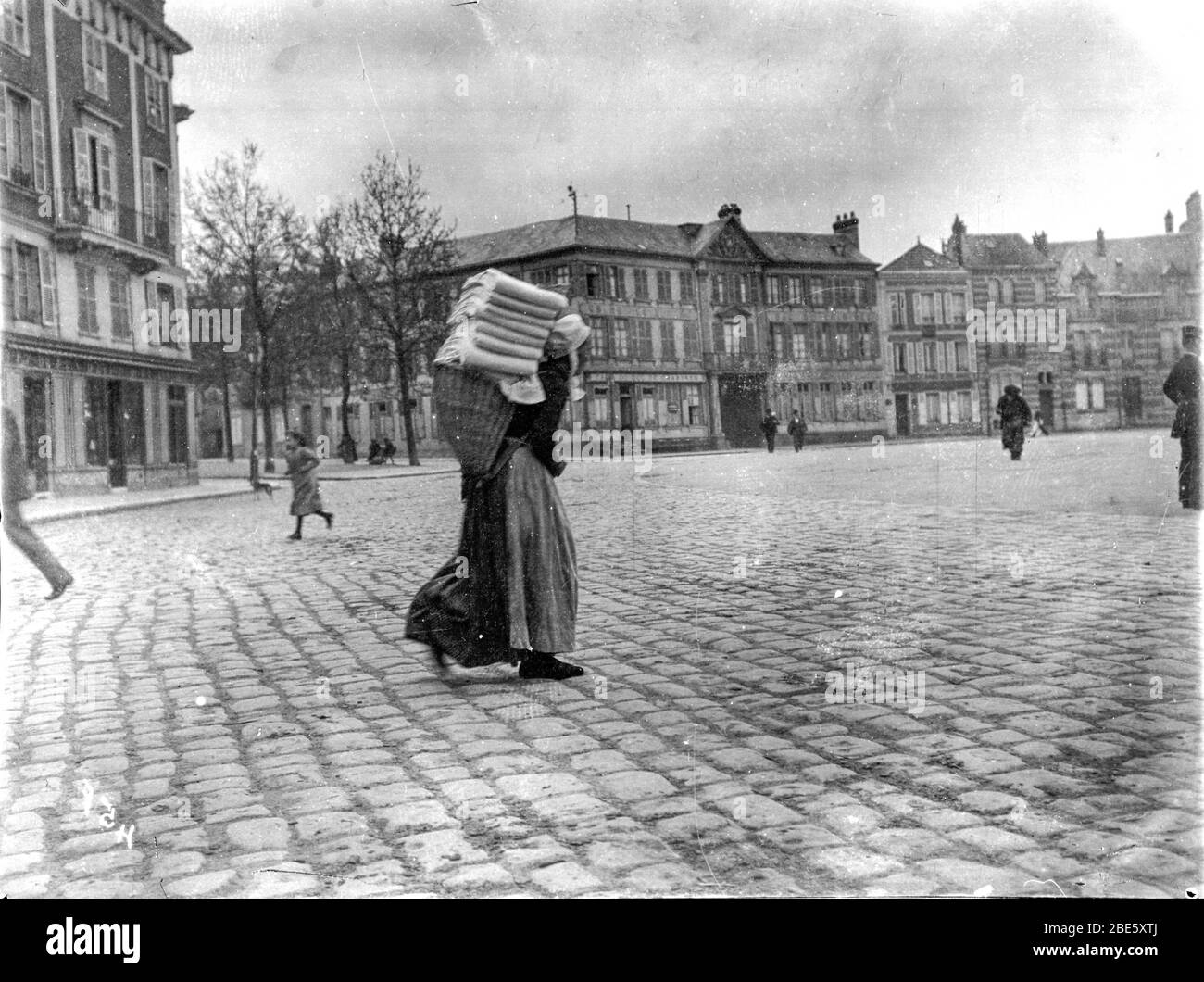 Une vieille dame porte un panier de lessive sur son dos à travers les rues pavées de Dieppe dans les années 1890 Banque D'Images
