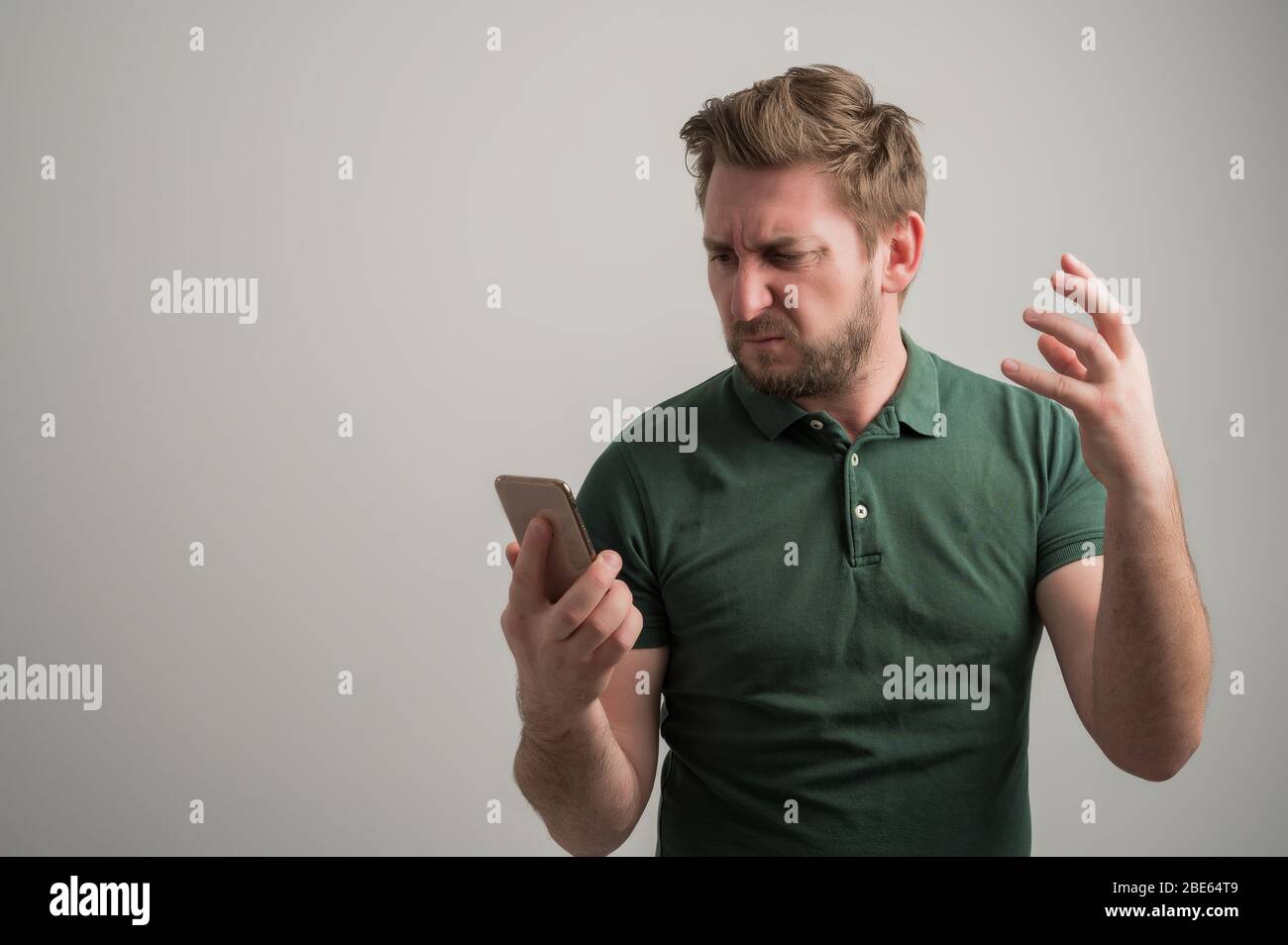 Portrait d'un homme élégant et sérieux avec barbe épaisse, vêtu d'un t-shirt vert décontracté utilisant des applications mobiles textant sur téléphone portable isolé o Banque D'Images