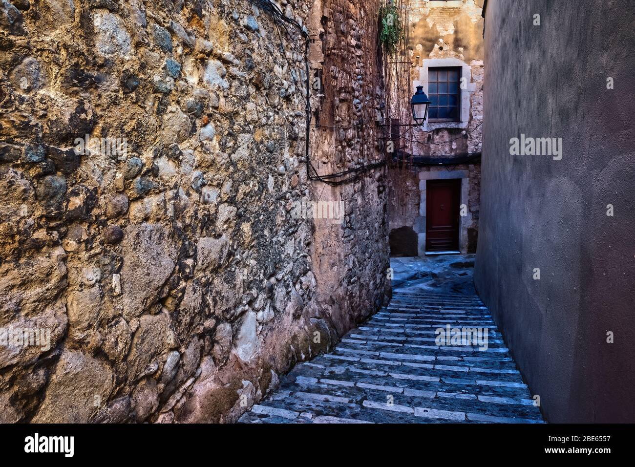 Allée avec des marches le long de vieux mur médiéval en pierre dans la vieille ville, le quartier juif - El Call dans la ville de Gérone en Catalogne, Espagne Banque D'Images