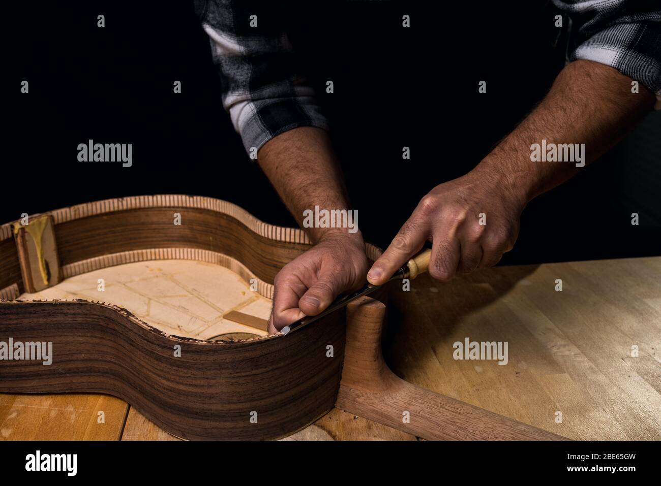 Homme faisant une guitare. Mains dans le maillot de secours en bois. Outil gouge. Fond noir foncé Banque D'Images