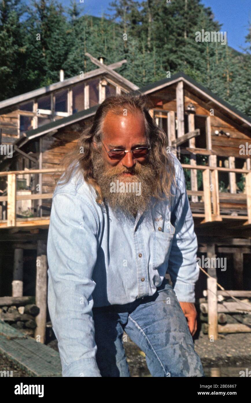 Un homme senior avec une barbe longue tient un bateau à l'extérieur d'un pavillon en bois, Sadie Cove, Homer, Alaska, États-Unis Banque D'Images