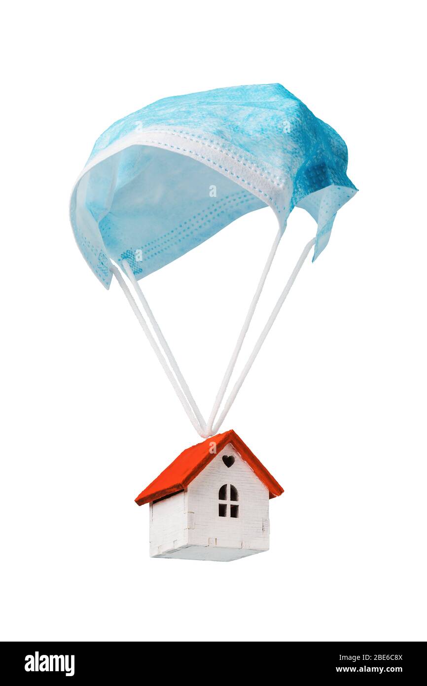 Une maison de jouets vole sur un parachute à partir d'un masque médical, isolé sur un fond blanc. Le concept d'une maison protégée contre le coronavirus et autres v Banque D'Images