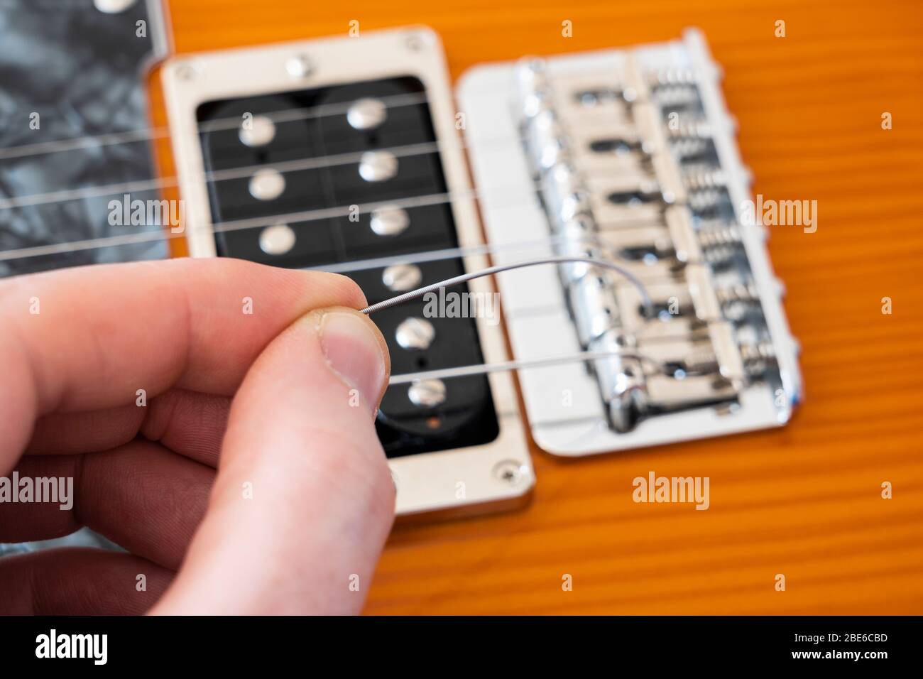 Changer la chaîne sur une guitare électrique Fender Modern Player Telecaster en tirant une nouvelle chaîne à travers une selle sur le pont arrière rigide vintage Banque D'Images