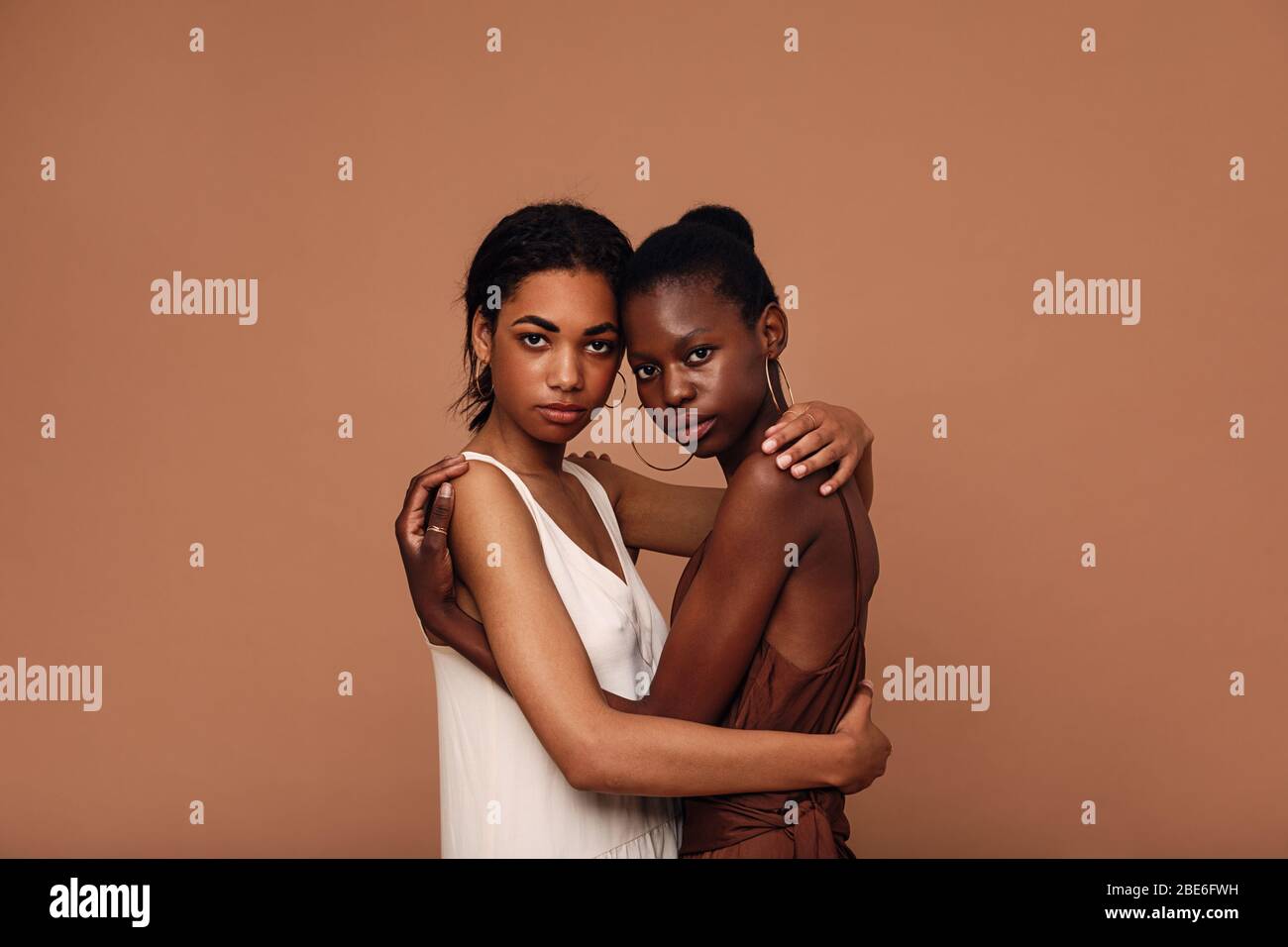 Deux femmes amis diverses contre fond brun se embrassant Banque D'Images