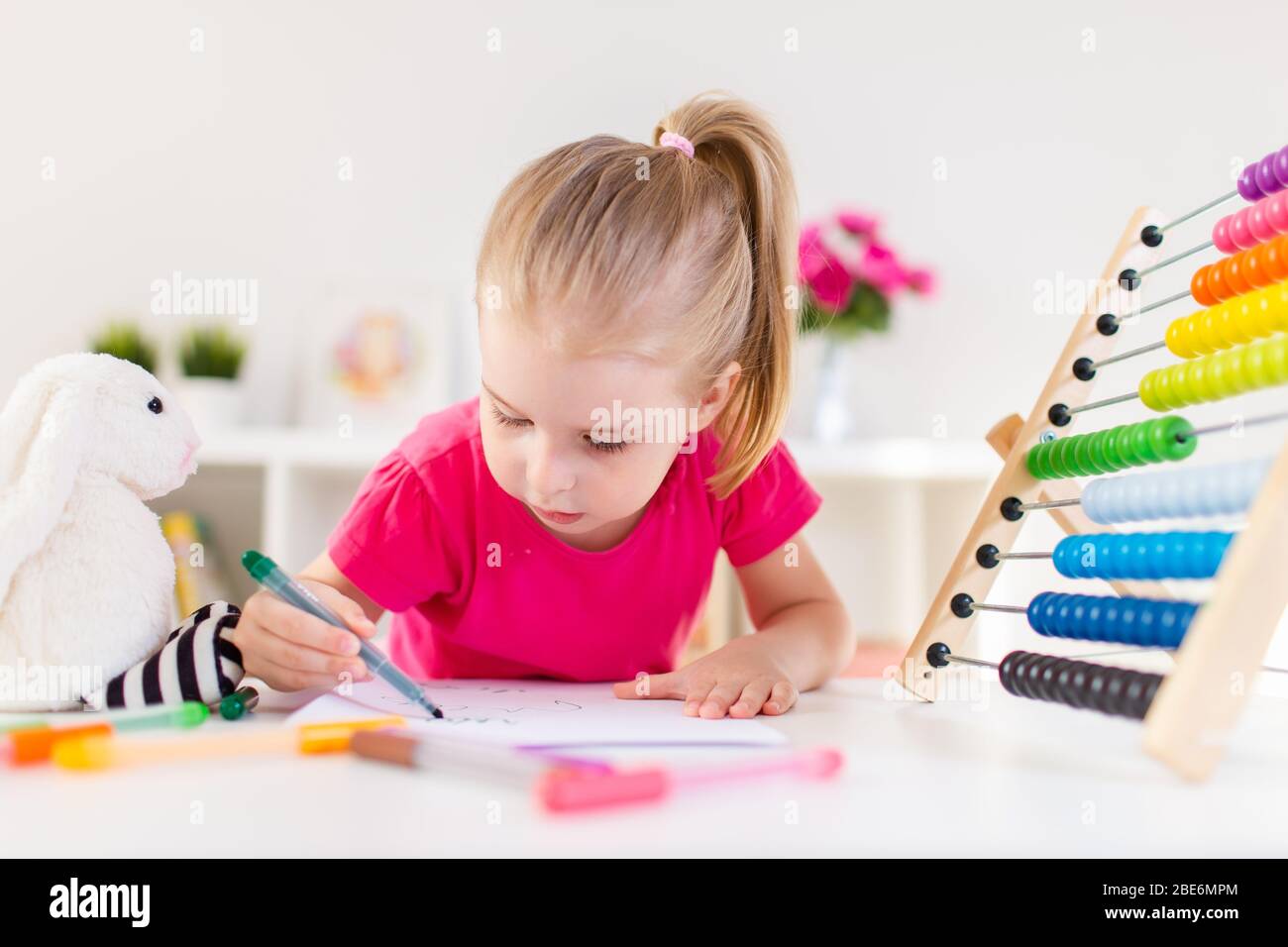 Blonde bonne fille dessin et écriture siitting par la table blanche dans la salle de lumière avec abacus en bois coloré. Éducation préscolaire, apprentissage précoce Banque D'Images