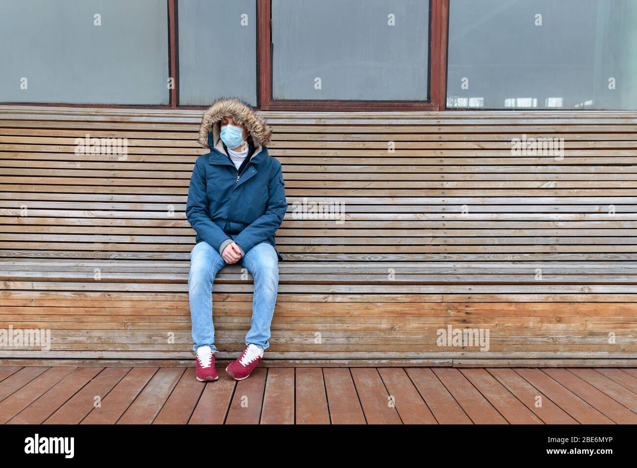 Homme malade avec une cagoule assise seule sur un banc, portant un masque facial contre les maladies infectieuses transmissibles, covid-19. Ville vide des gens en raison de la coro Banque D'Images
