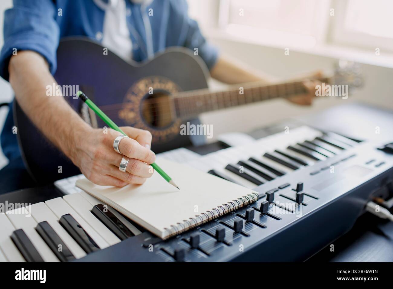 Arrangeur de musique masculine composant la chanson sur le piano midi et  l'équipement audio dans le studio d'enregistrement numérique. L'homme joue  de la guitare et produit une bande-son électronique Photo Stock -