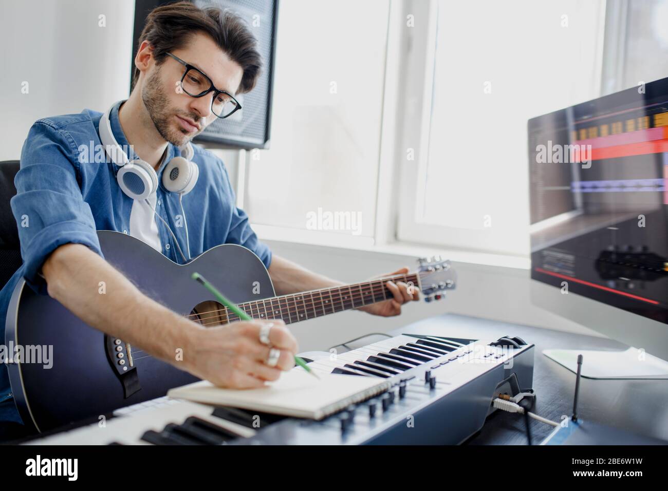 Arrangeur de musique masculine composant la chanson sur le piano midi et  l'équipement audio dans le studio d'enregistrement numérique. L'homme joue  de la guitare et produit une bande-son électronique Photo Stock -