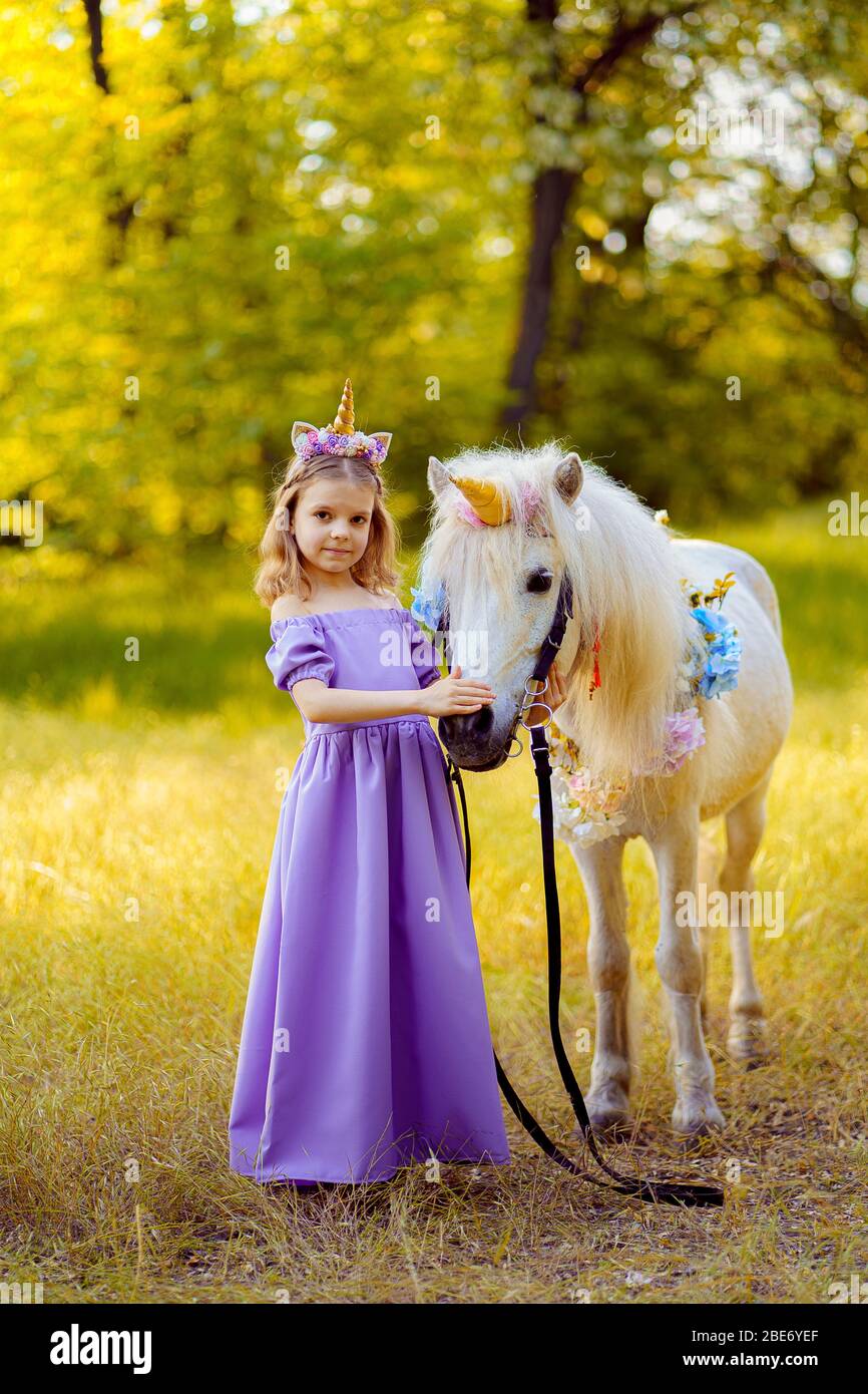 Fille en robe violette avec couronne d'une licorne dans les cheveux embrassant le cheval blanc unicorn. Les rêves deviennent réalité. Conte de fées. Banque D'Images