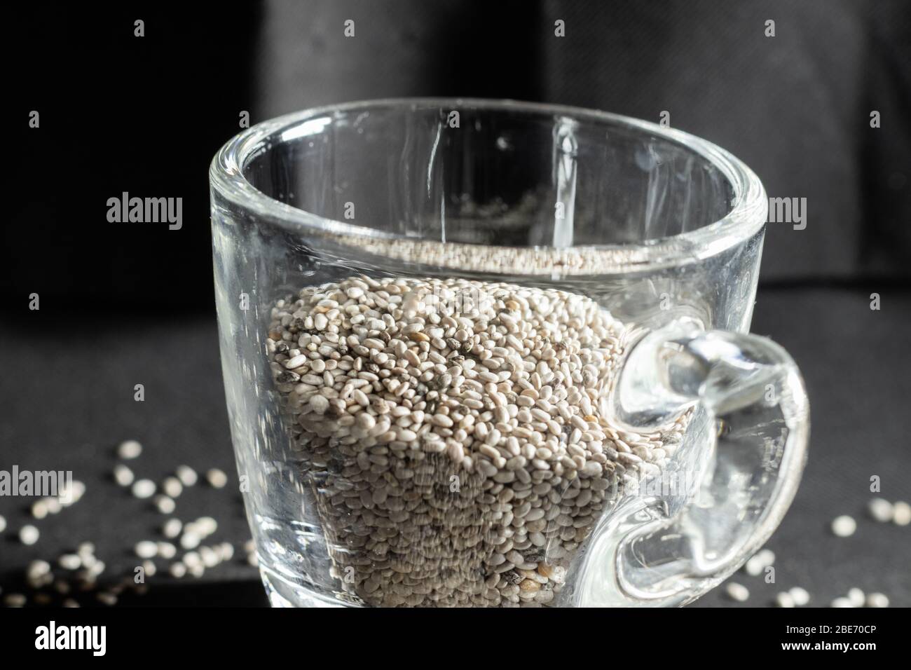 Gros plan de graines de chia blanc biologique, dans un petit mug en verre sur fond noir Banque D'Images