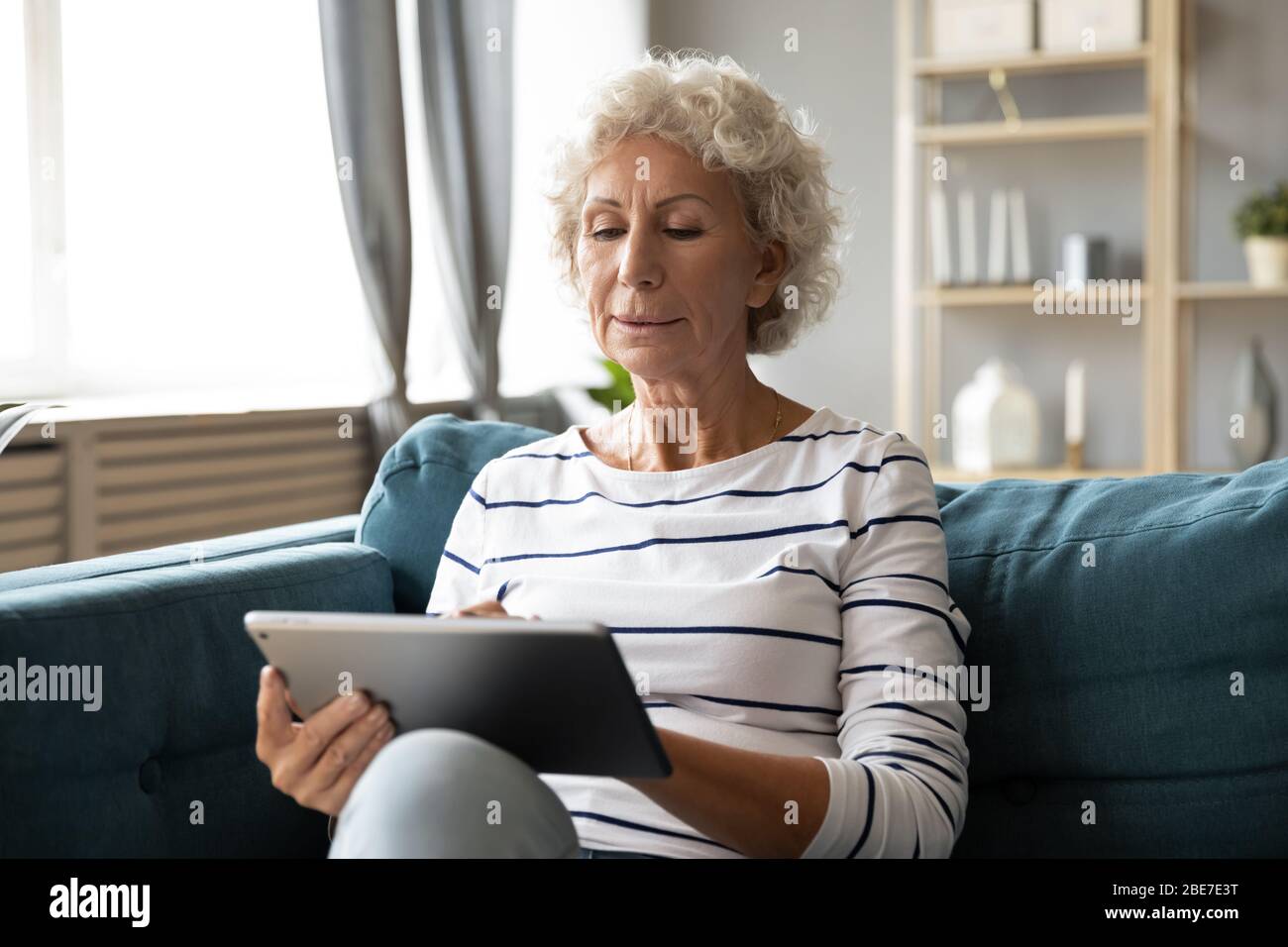 Satisfait focalisé femme âgée utilisant la tablette d'ordinateur, regarder l'écran Banque D'Images