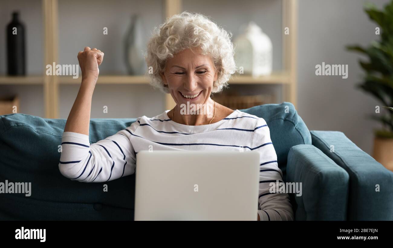 Une femme âgée et excitée regardant l'écran d'un ordinateur portable, se réjouit de la victoire Banque D'Images