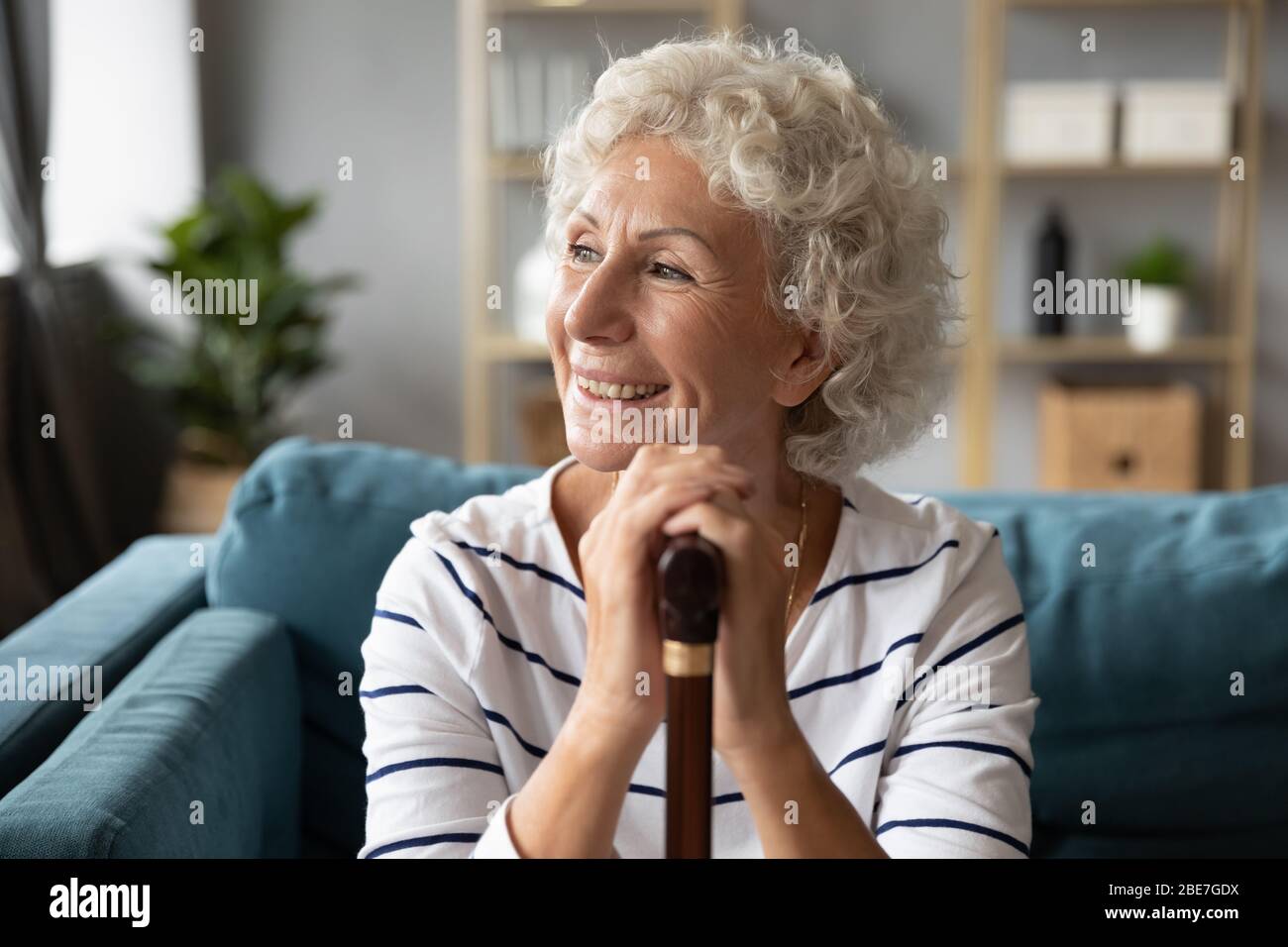 Heureuse femme âgée souriante tenant les mains sur la canne en bois Banque D'Images