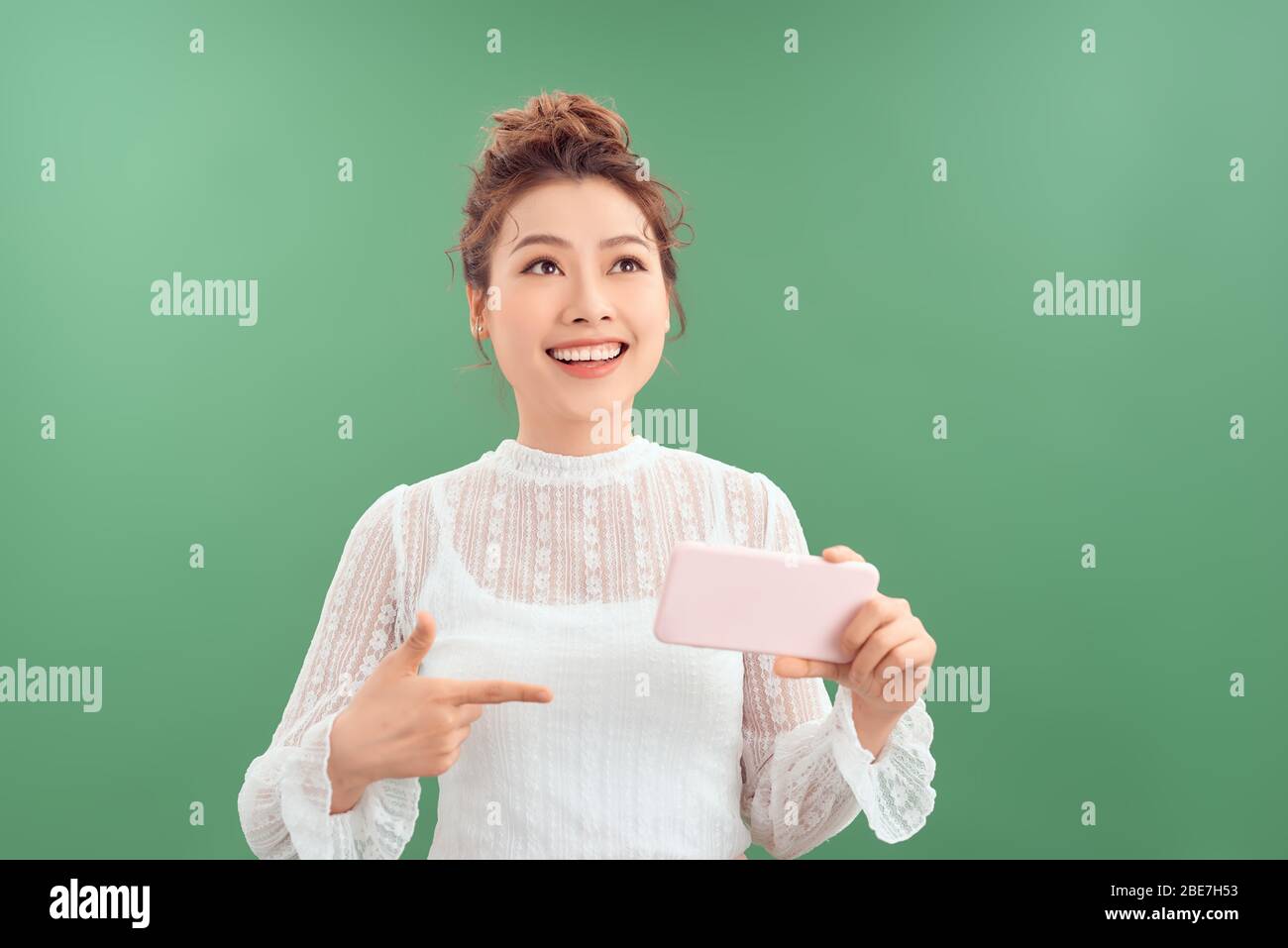 Belle jeune femme asiatique montrant le téléphone mobile tout en se tenant et en regardant isolé sur fond vert. Banque D'Images