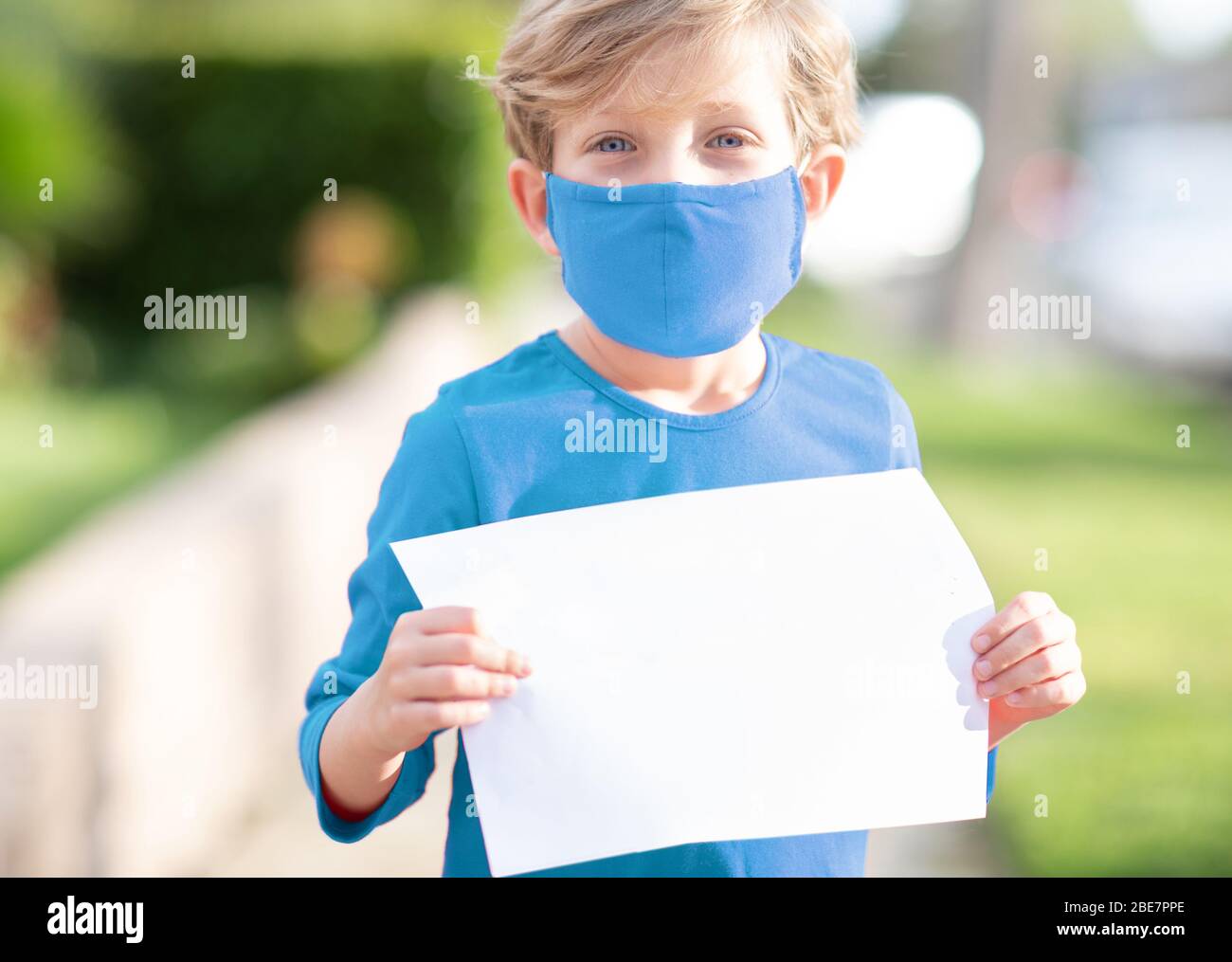 Un petit garçon dans un masque de visage en tissu tenant un message pendant la crise mondiale de covid-19 de la pandémie de coronavirus Banque D'Images