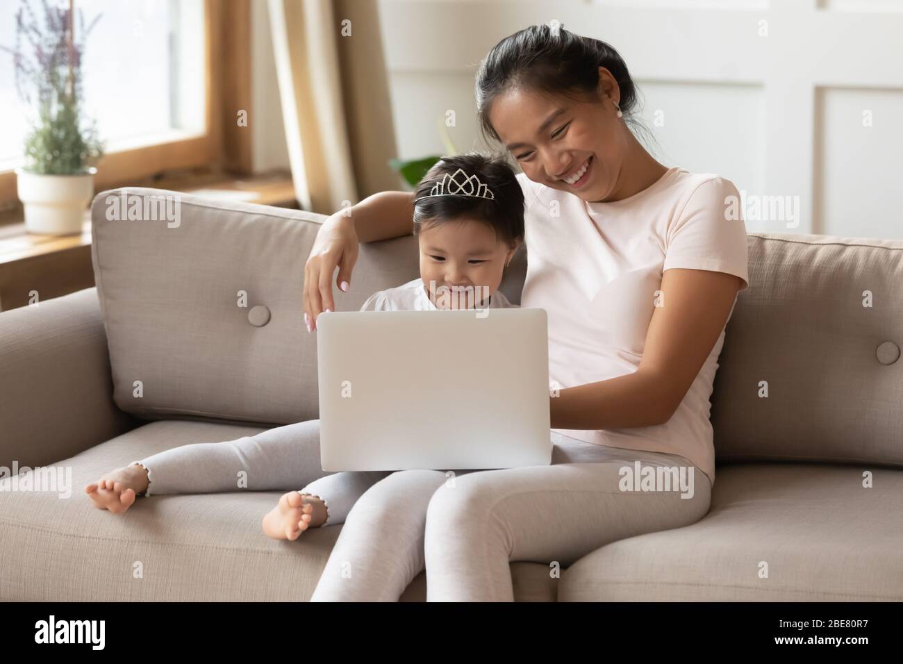 Fille de mère asiatique assise sur le canapé regarder des dessins animés sur ordinateur portable Banque D'Images