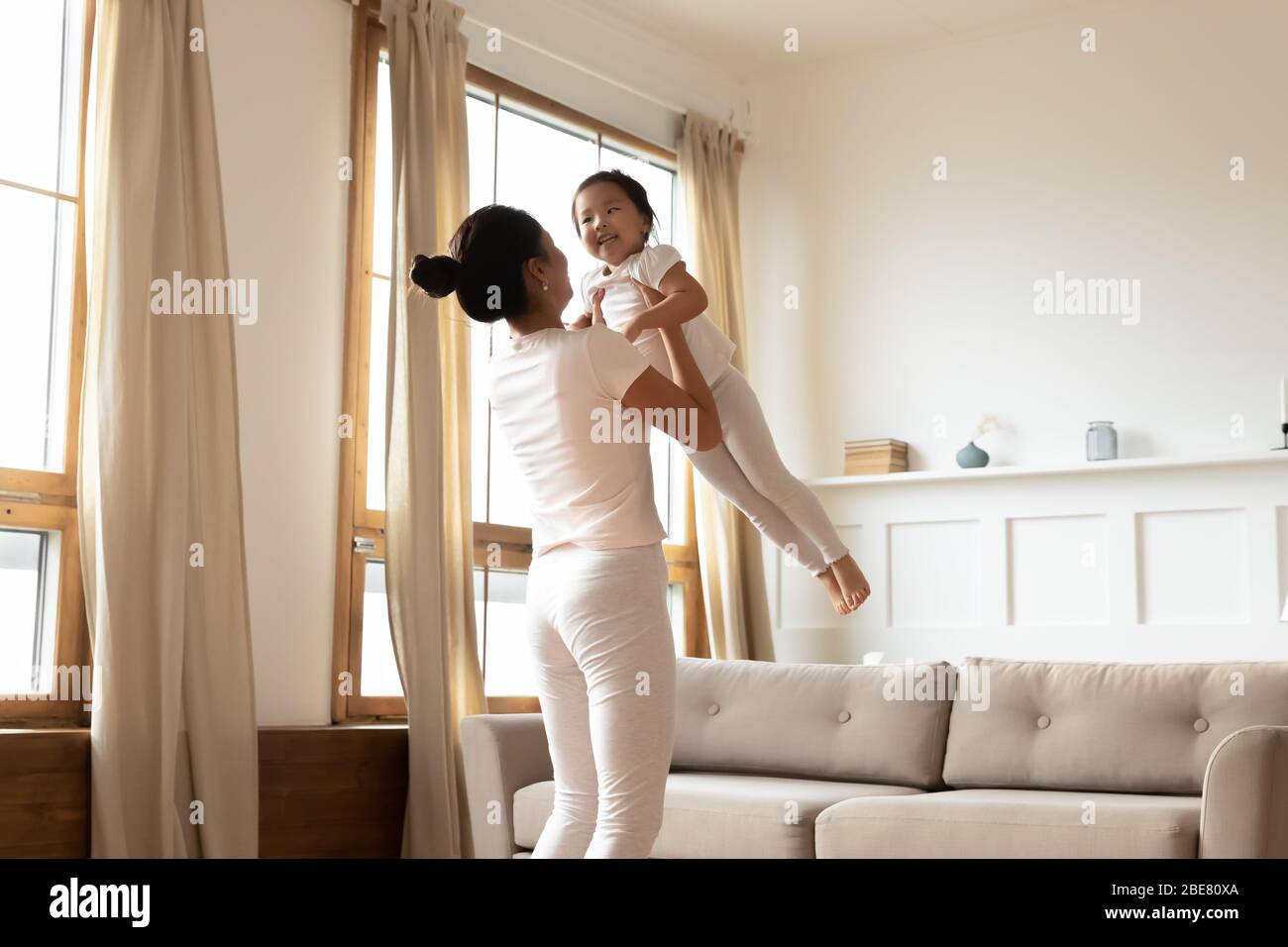 Maman joue avec une petite fille asiatique la soulevant et se balançant Banque D'Images
