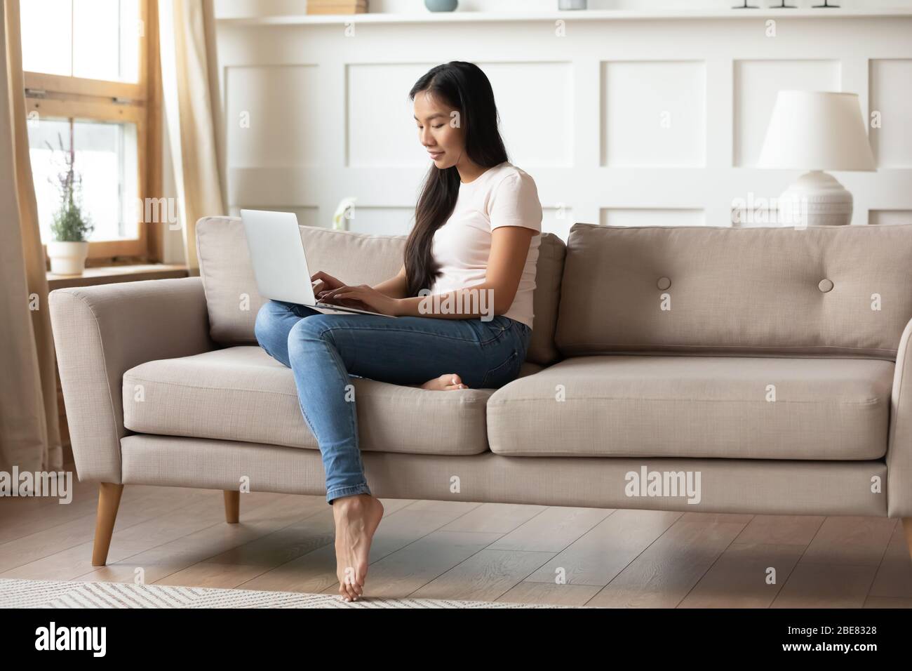 Dans le salon vietnamienne femme utilisant un ordinateur portable assis sur un canapé Banque D'Images