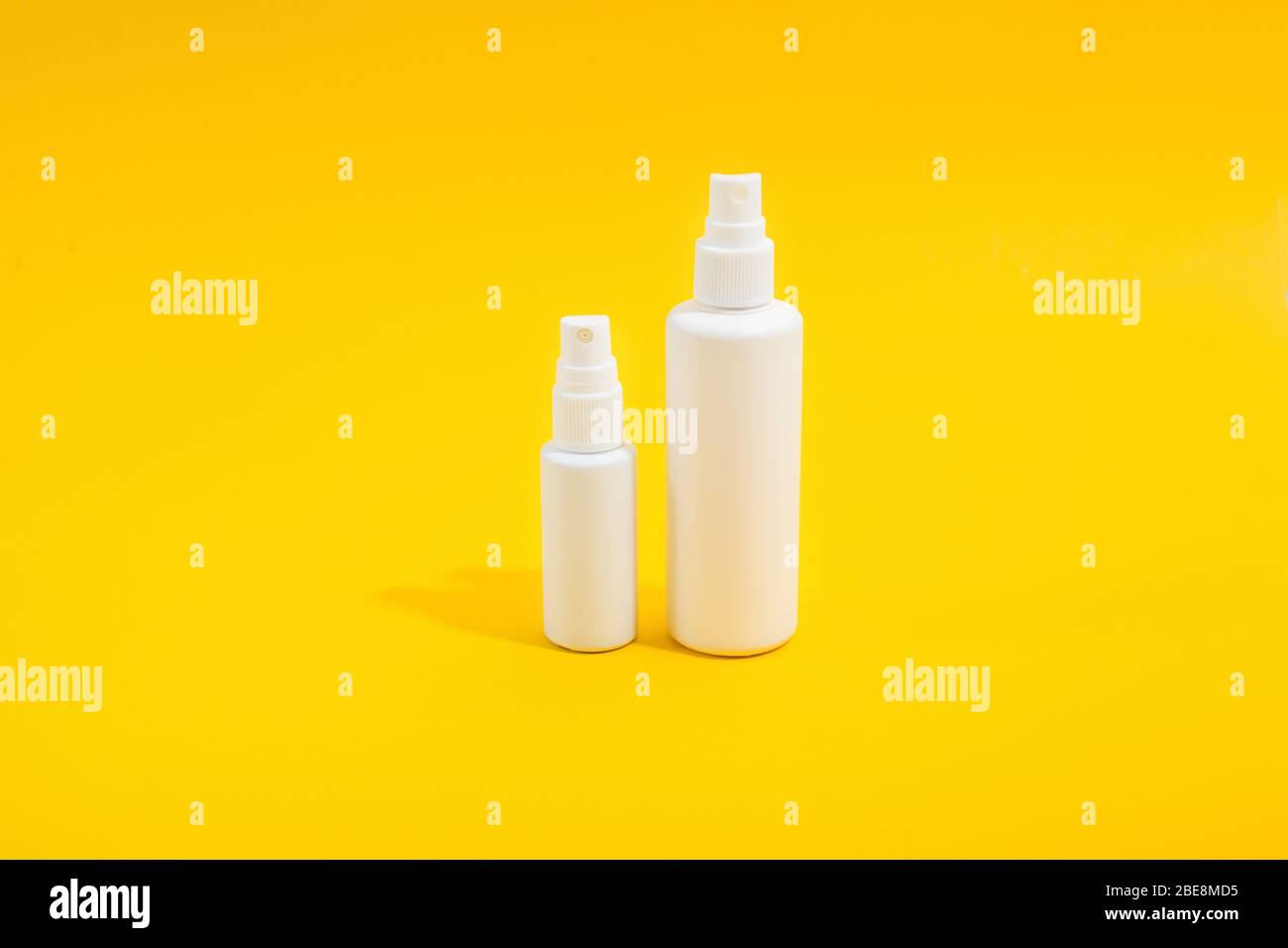 Deux bouteilles en plastique blanc avec vaporisation sur fond jaune. Solution désinfectante pour la maison et mini-version pour sac à main. Espace de copie. Maquette pour la conception Banque D'Images