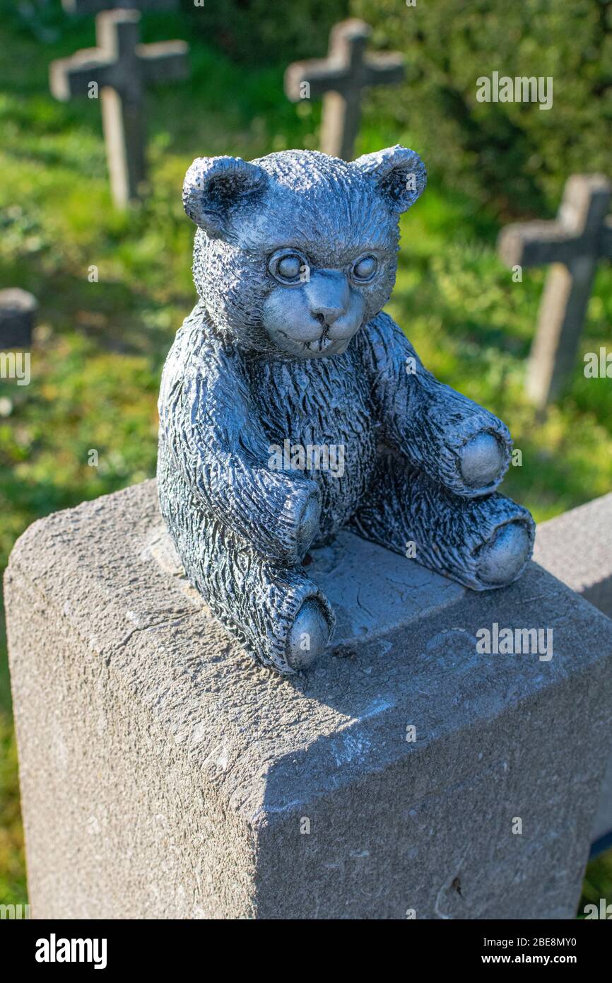 Statue en béton d'un petit ours peint en argent avec de petites croix en béton en arrière-plan Banque D'Images