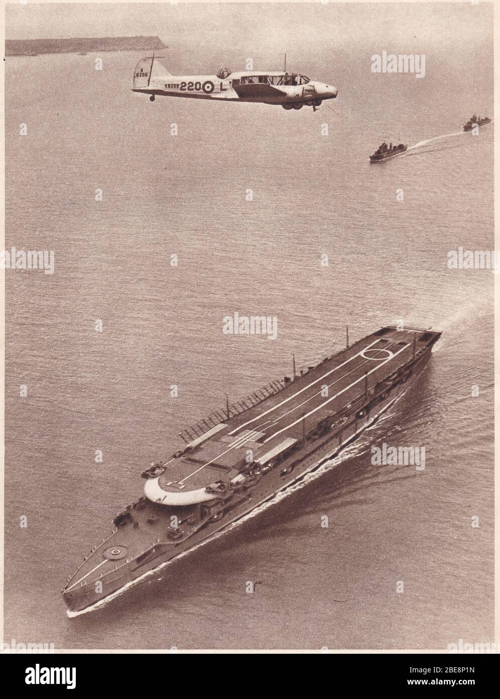 Photo noir et blanc vintage des années 1930 d'un avion Avro Anson survolant le porte-avions H.M.S. Furieux en mer. Banque D'Images