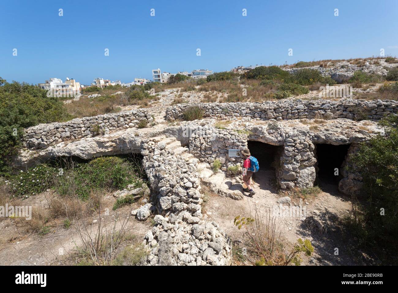 Grottes de logements possibles de l'ère puniques avec un panneau d'information de lecture personne, Xemxija, Malte Banque D'Images