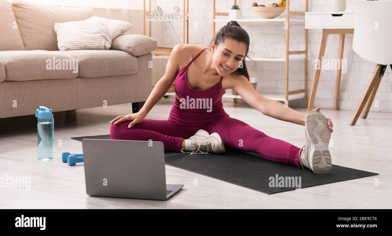 Rester actif pendant l'auto-isolation. Belle fille qui s'étire et regarde la vidéo sur un ordinateur portable à la maison. Panorama Banque D'Images