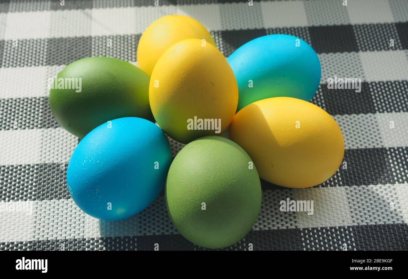 Les œufs de Pâques colorés se trouvent sur une nappe à carreaux. Œufs jaunes, bleus et verts. La vie-fixe. Banque D'Images