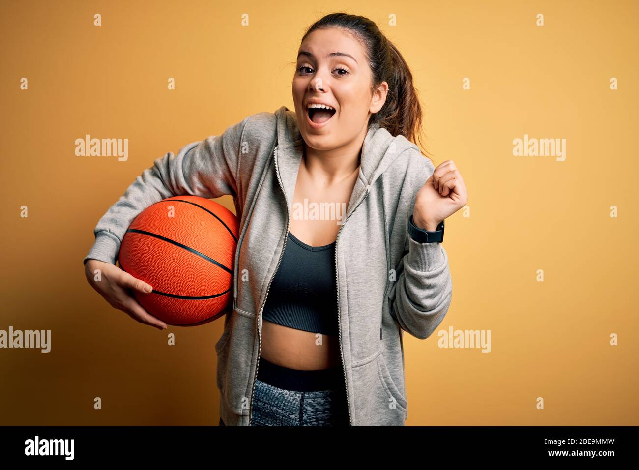 Jeune homme sportif brunette qui tient un ballon de basket-ball sur fond  jaune criant fier et célébrant la victoire et le succès très excité Photo  Stock - Alamy