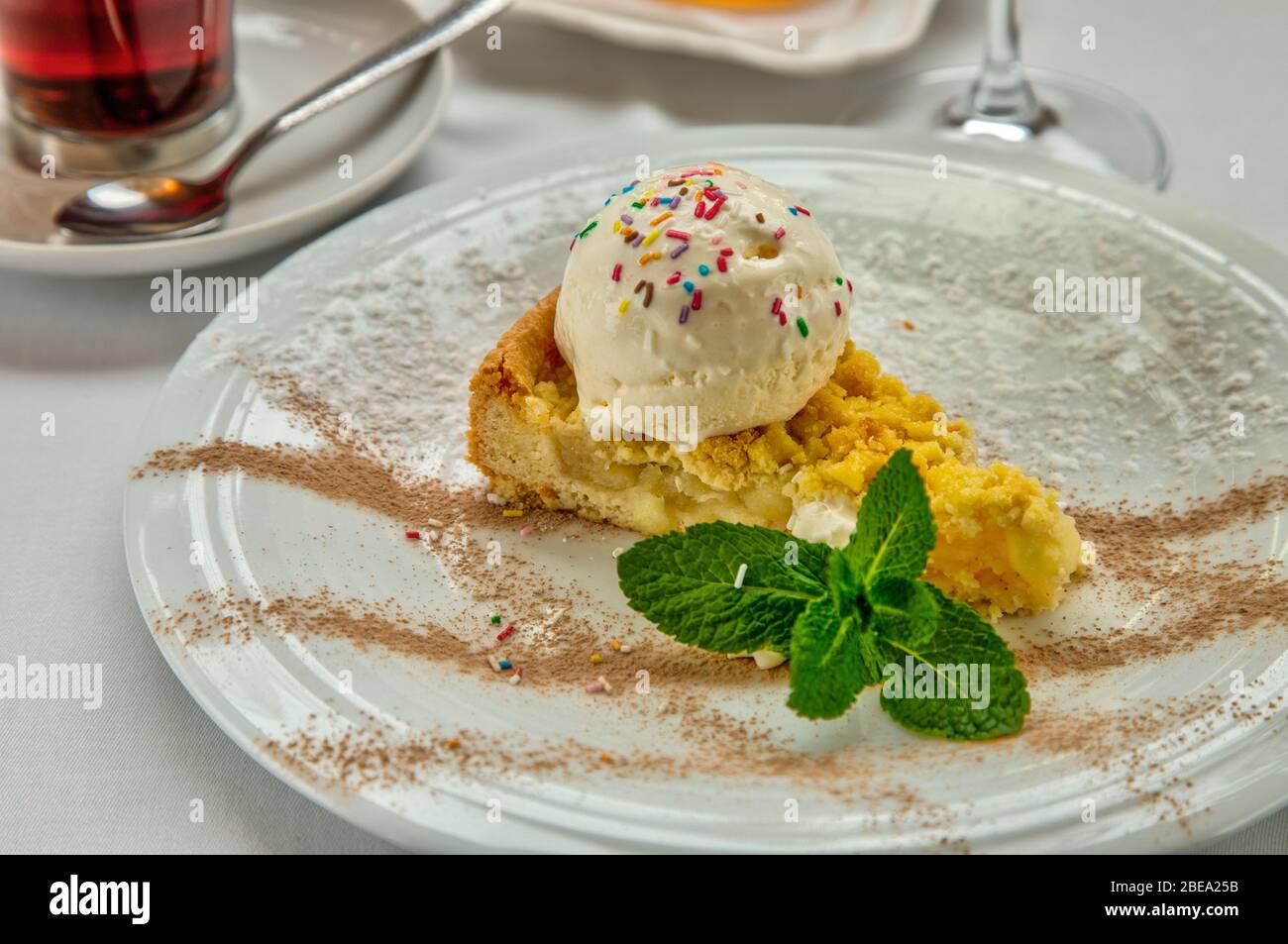 Morceau De Gateau Charlotte Avec Des Pommes Boule De Creme Glacee Et De Menthe Fraiche Sur La Plaque Blanche Servi Avec Une Rosette De Miel Une Tasse De The Aromatique Et Un Morceau De Gateau Charlotte Avec Des Pommes Boule De Creme Glacee Et De Menthe Fraiche Sur La Plaque Blanche Servi Avec Une Rosette De Miel Une Tasse De The Aromatique Et Un