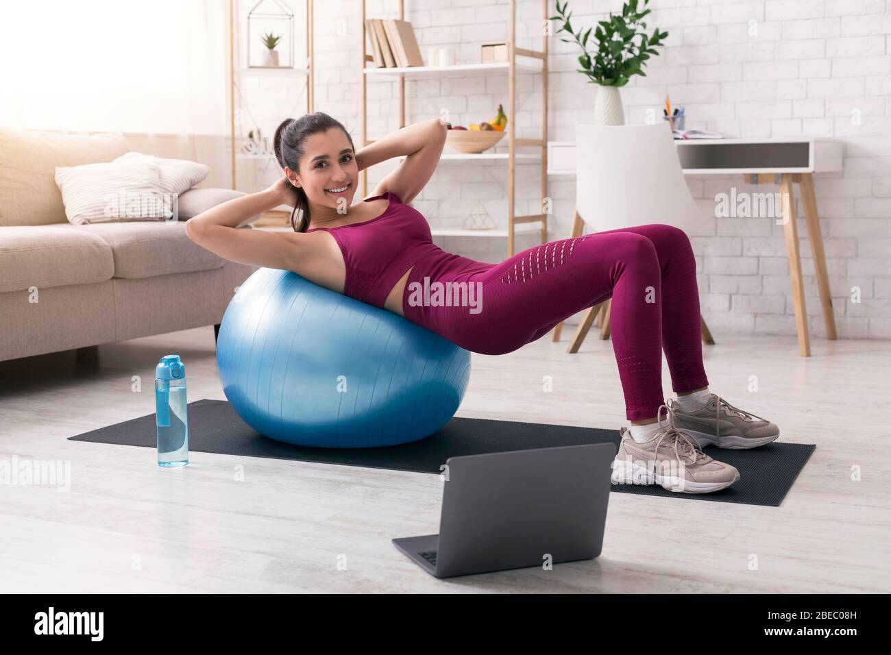Restez à la maison, restez actif. Femme hispanique qui travaille avec un ballon de fitness près d'un ordinateur portable dans le salon Banque D'Images