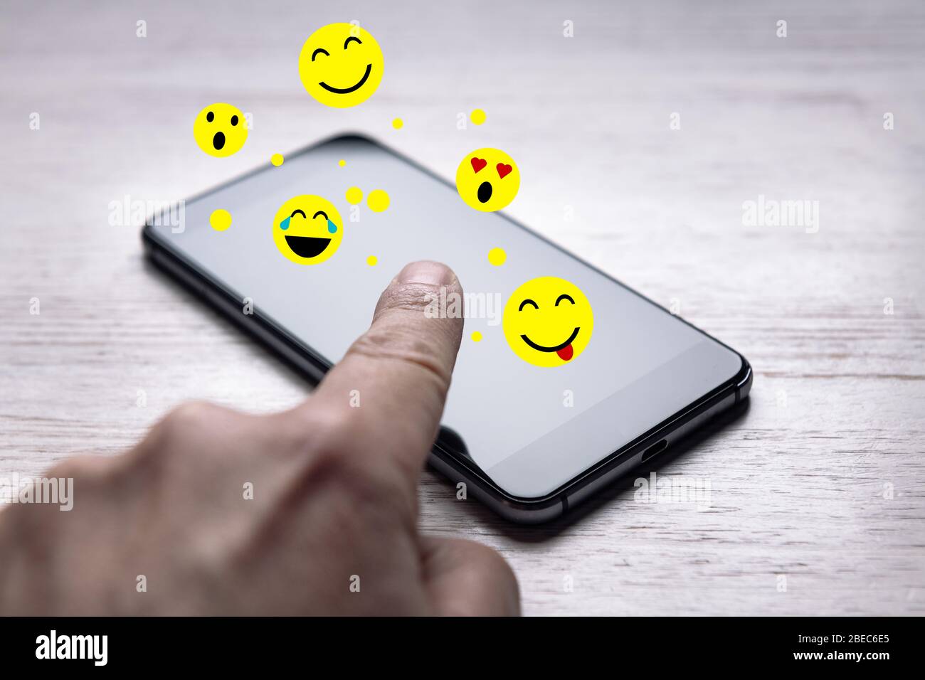 toucher l'écran d'un téléphone que les émoticônes sortent de sur la table en bois blanc, les médias sociaux et le concept de communication, copier l'espace pour le texte, s Banque D'Images