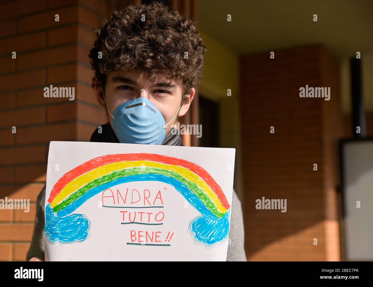 Turin,Piémont,Italie.Mars 2020.quarantaine de Cornonavirus.Portrait d'un garçon caucasien brun mauresque avec masque bleu et un dessin avec l'arc-en-ciel et le Banque D'Images