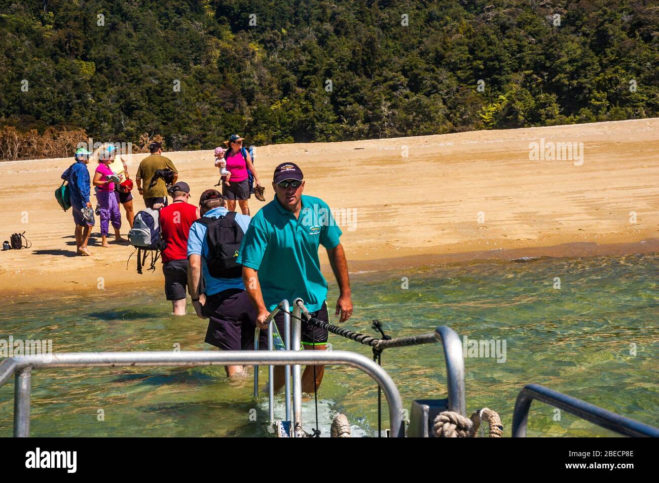 Day trippers patauger à terre d'une navette taxi de l'eau de mer sur une plage dans le parc national Abel Tasman, île du Sud, Nouvelle-Zélande. Banque D'Images