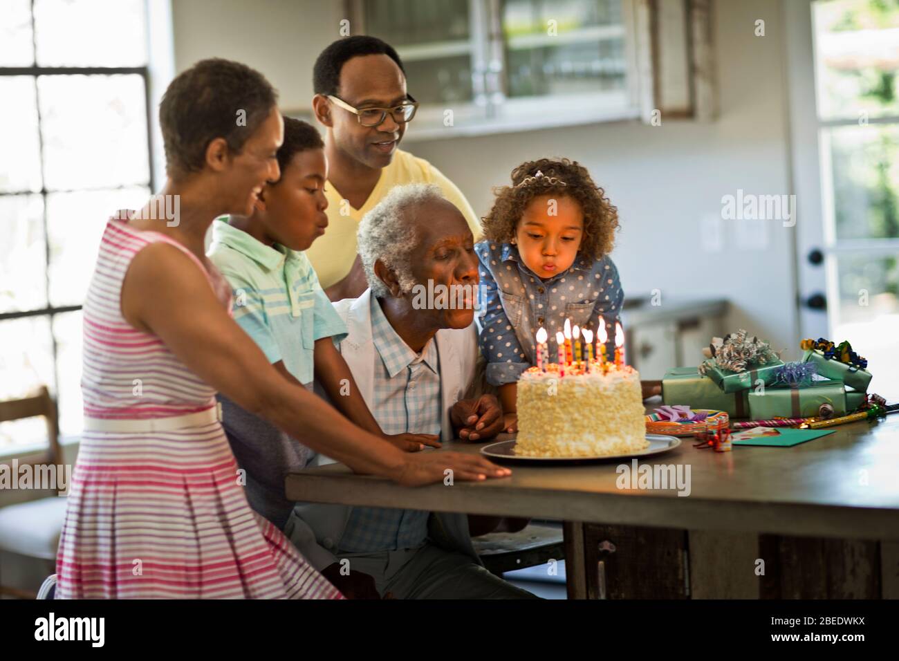 Homme senior qui souffle des bougies sur son gâteau d'anniversaire avec ses petits-enfants lors d'une réunion de famille Banque D'Images