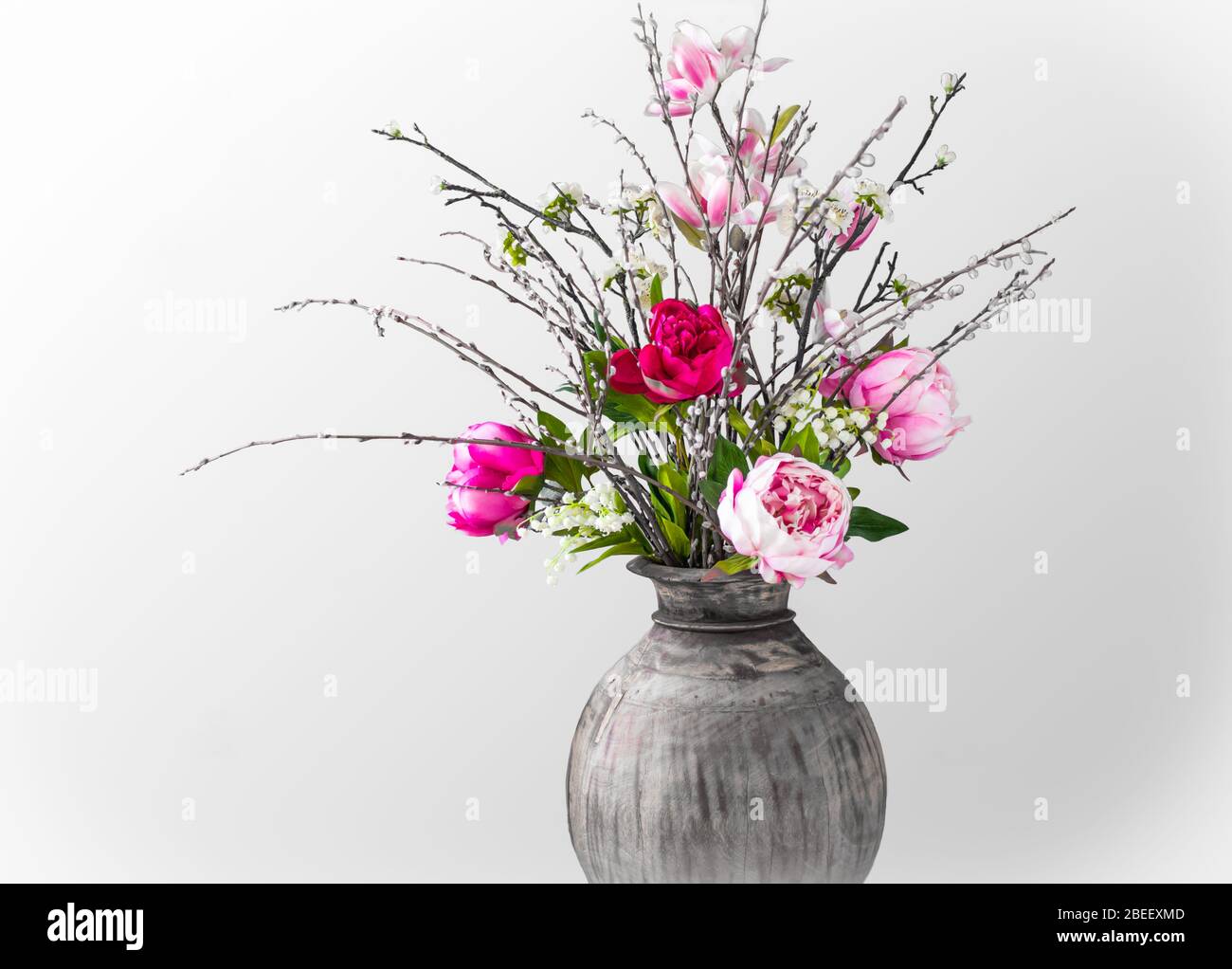 Bouquet de printemps moderne sauvage avec pivoines roses, branches de magnolia, cloches de mai et chatons de saules sur fond blanc. Gros plan. Banque D'Images