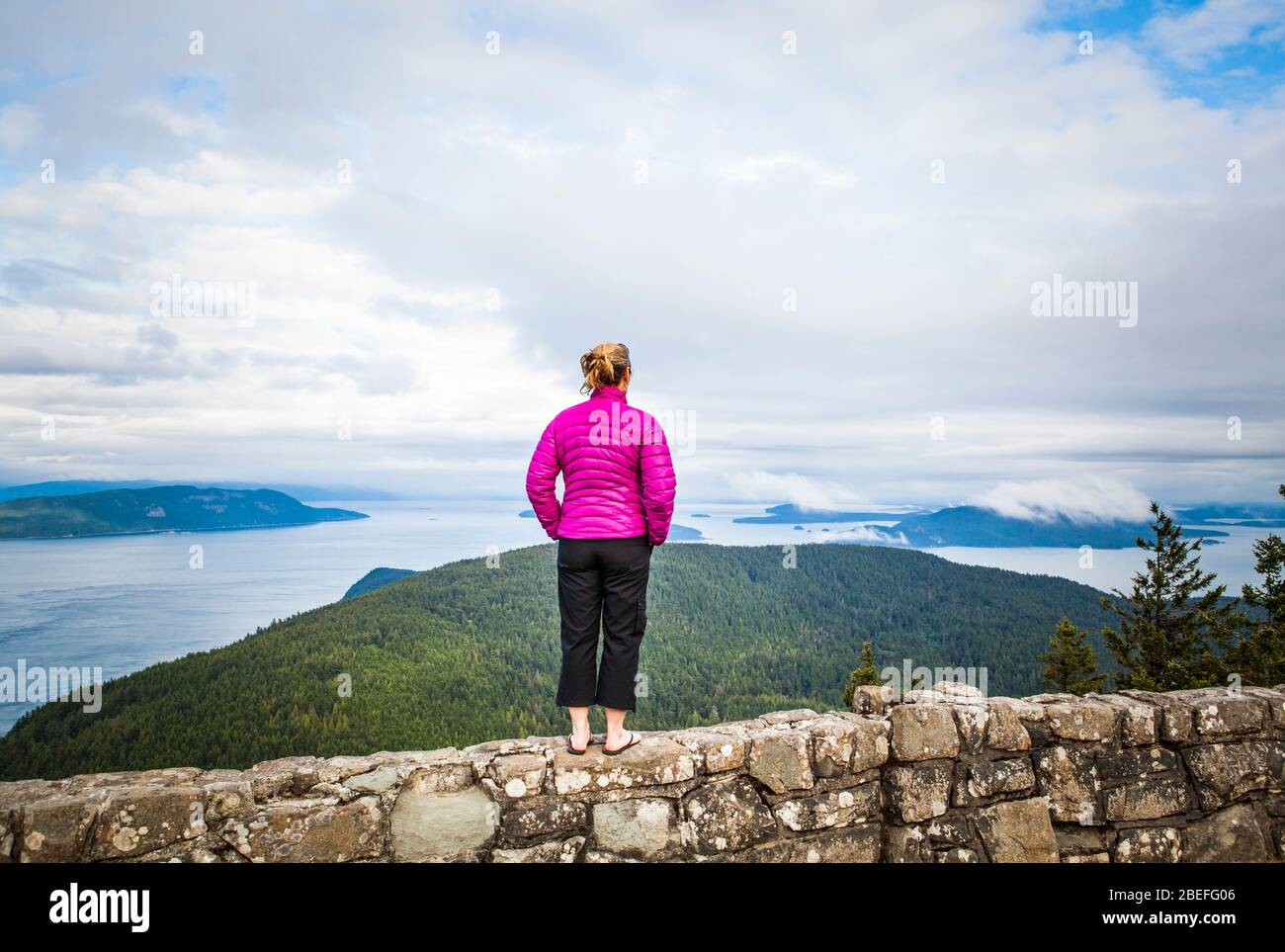 Une femme debout au sommet d'un mur de roche au sommet du mont Constitution dans le parc national de Moran, Orcas Island, Washington, États-Unis. Banque D'Images