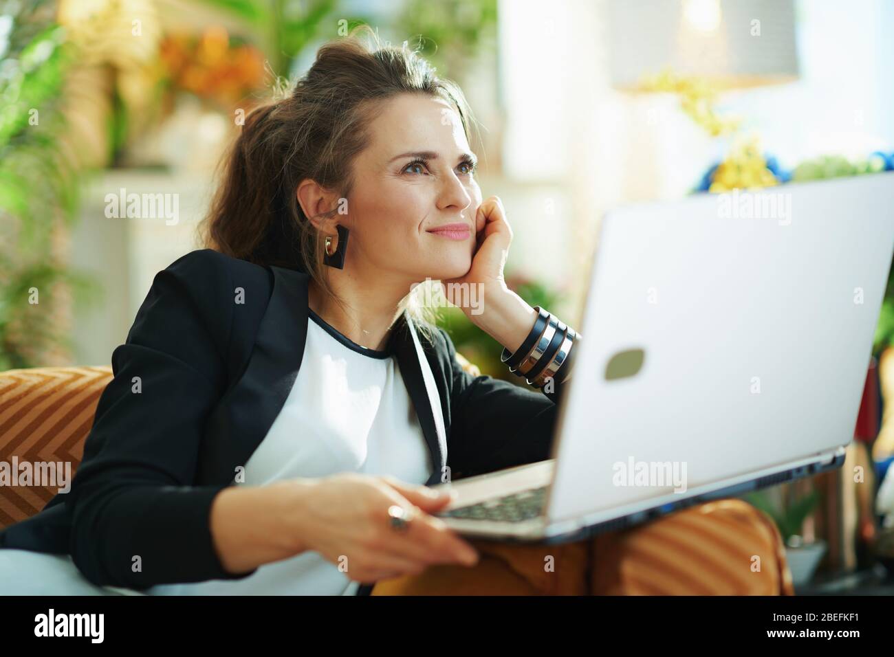 pensif élégant foyer d'âge moyen dans la blouse blanche et veste noire dans la maison moderne en journée ensoleillée en regardant la distance et lire le texte sur un Banque D'Images